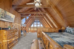 Eine Blockhütte mit Schlafzimmer im oberen Bereich, Holzmöbeln und einem Deckenventilator.