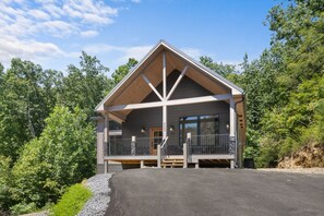 Une cabane en rondins à deux étages, dotée d’un porche, d’une porte d’entrée et d’une grande fenêtre.
