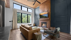 A modern living room with a large window, a fireplace, and a ceiling fan. - On The Rocks|Luxury Mtn Cabin w/ Indoor Pool (Sevierville)