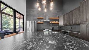 A modern kitchen with a large island, dark countertops, and a hanging light fixture. - On The Rocks|Luxury Mtn Cabin w/ Indoor Pool (Sevierville)