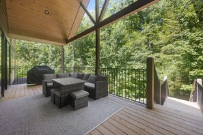 Une terrasse extérieure couverte avec un plafond en bois, un barbecue intégré et un espace salon comprenant une table et des canapés.