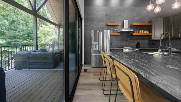 A modern kitchen with a large island, stainless steel appliances, and a view of a wooden deck and outdoor seating area. - On The Rocks|Luxury Mtn Cabin w/ Indoor Pool (Sevierville)