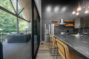 Una cocina moderna con una isla grande, electrodomésticos de acero inoxidable y vistas a una terraza de madera con mobiliario exterior.