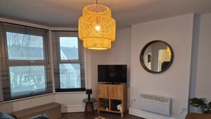 En moderne stue med en sofa, et fjernsyn på et træstel, et rundt spejl og en hængende lampe.