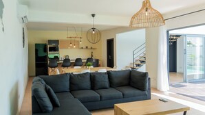 A modern living room with a sectional sofa, a wooden coffee table, and a dining area with a kitchen in the background. - Villa Aaya Grand Baie, Private Pool,3 Bedrooms, 7 mins to Pereybere beach (Moka District)