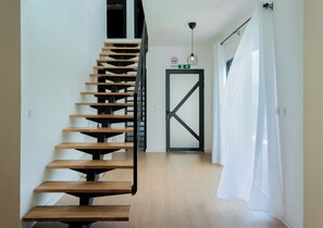 Uma escada moderna com degraus de madeira e guarda-corpo de metal, que leva a uma porta com o aviso "No Smoking" acima.