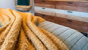 Una camera da letto con un letto, una poltrona sospesa, un televisore e un comò in legno.