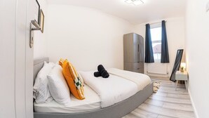 Quarto com cama curva, guarda-roupa, mesa de cabeceira com abajur e janela com cortinas.