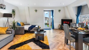 A modern living room with a sofa, a dining table set for two, a TV, and a balcony with a view.