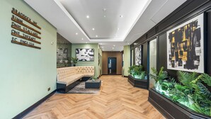 A modern hallway with a herringbone floor, a sectional sofa, and a glass display case with plants.