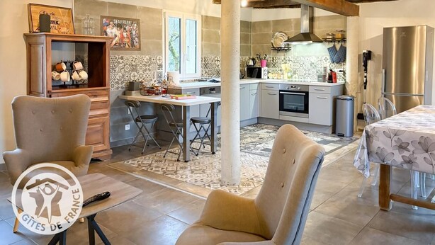 A rustic kitchen with exposed wooden beams, a dining area with two chairs, a small table, and a kitchen counter with appliances. - Gîtes de France® - Héloïse's gîte (BETAILLE)