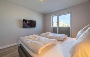 Et moderne hotelværelse med to senge, et fladskærms-tv ophængt på væggen og et stort vindue med udsigt over byen.