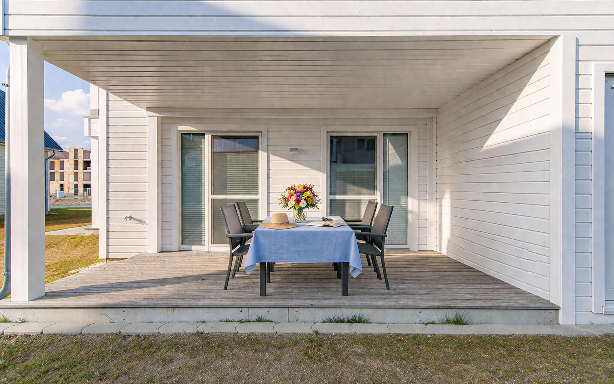 A covered outdoor patio with a table set for two, a vase of flowers, and a view of the surrounding area.
