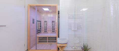 A modern bathroom with a glass shower enclosure, a wooden vanity, and a potted plant.