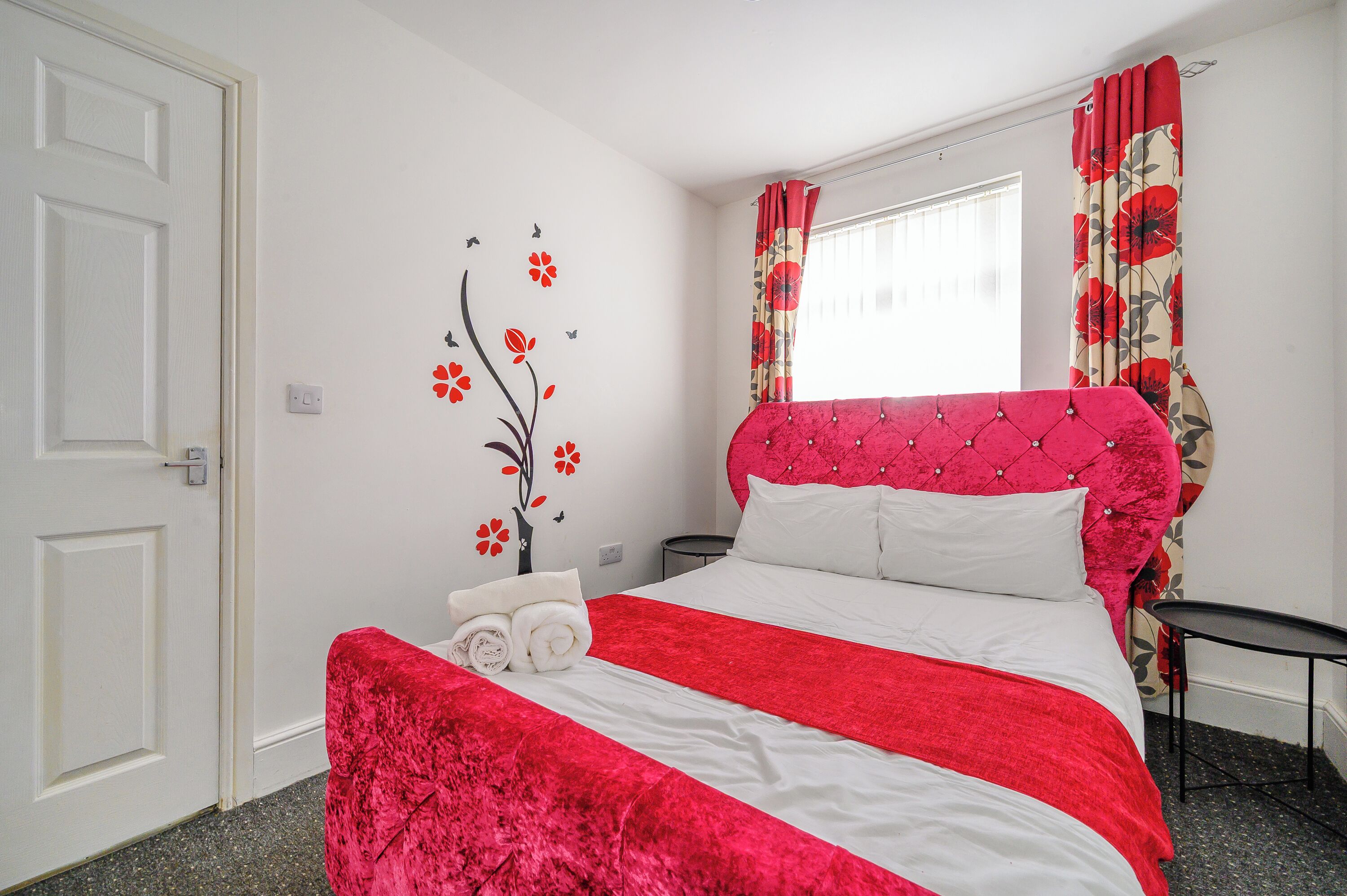 A neatly made bed with a red and white bedspread, a tufted headboard, and a small bedside table with a lamp.
