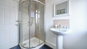 Een moderne badkamer met een douchecabine van glas, een wit wastafelmeubel en een afbeelding in een lijst aan de muur.