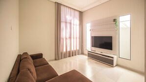 A modern living room with a large flat-screen TV, a brown sectional sofa, and a sliding glass door with curtains.