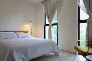 Ein Schlafzimmer mit Bett, Stuhl, Lampe und einem Fenster mit Vorhängen.