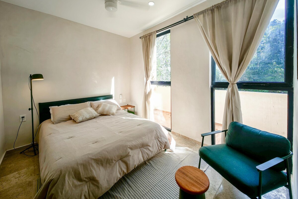 Ein Schlafzimmer mit einem Bett, einem grünen Sessel, einer Stehlampe und einem Fenster mit Vorhängen.