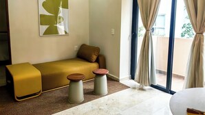 Et moderne værelse med sofa, to skamler, et stort vindue med gardiner, en klimaanlæg og et billedværk på væggen.