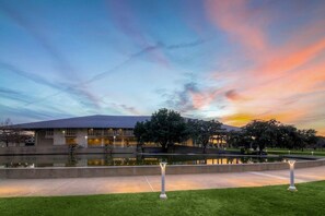 A modern building with a large reflective pool, surrounded by well-maintained grass and trees. - Texas Ranch Retreat | Fun Backyard + Firepit (Austin)