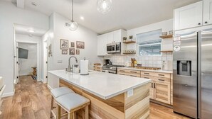 Eine moderne Küche mit einer zentralen Kochinsel, Edelstahlgeräten, Holzschränken und einer weißen Arbeitsplatte.