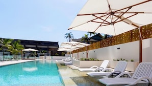 A swimming pool with lounge chairs and umbrellas, surrounded by a modern building with palm trees. - Ruby 30F Sunset Penthouse | Ocean & City Views (Surfers Paradise)