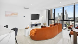 A modern living room with a large window, a flat-screen TV, and a sofa. - Ruby 30F Sunset Penthouse | Ocean & City Views (Surfers Paradise)