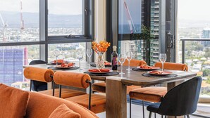 A dining area with a table set for four, large windows, orange upholstered chairs, and a view of the cityscape. - Ruby 30F Sunset Penthouse | Ocean & City Views (Surfers Paradise)