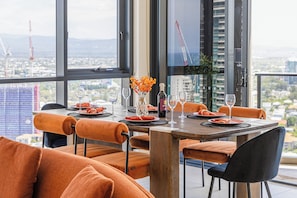 Ein Essbereich mit Tisch für vier Personen, großen Fenstern, orange gepolsterten Stühlen und Blick auf die Stadt.