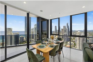 Un coin repas avec une table dressée pour quatre personnes, de grandes fenêtres offrant une vue sur la ville et un balcon doté d’une balustrade en verre.