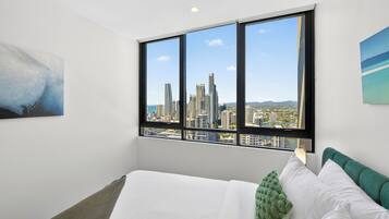 A hotel room with a large window offering a cityscape view, a neatly made bed, and a painting on the wall.