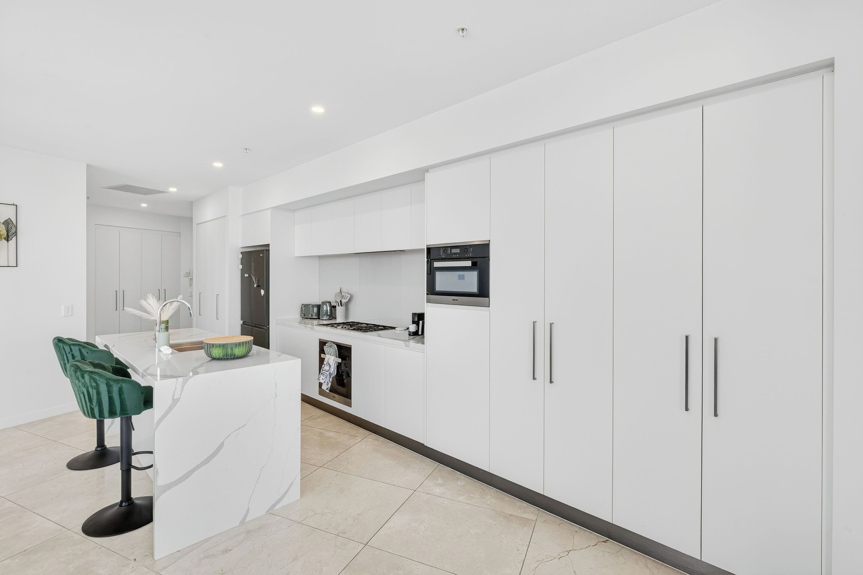 A modern kitchen with white cabinetry, a built-in microwave, and a central island with bar stools.