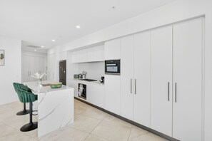 Une cuisine moderne avec des meubles blancs, un four à micro-ondes encastré et un îlot central doté de tabourets de bar.