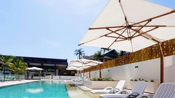 A swimming pool with lounge chairs and umbrellas, surrounded by a modern building with palm trees.