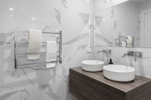 Une salle de bain moderne avec deux vasques, un meuble-lavabo en bois et une cabine de douche en verre.
