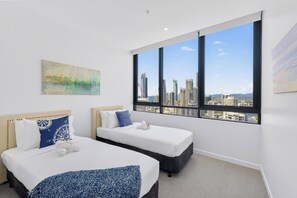 Une chambre d’hôtel avec deux lits, une grande fenêtre donnant sur la ville et un tableau accroché au mur.