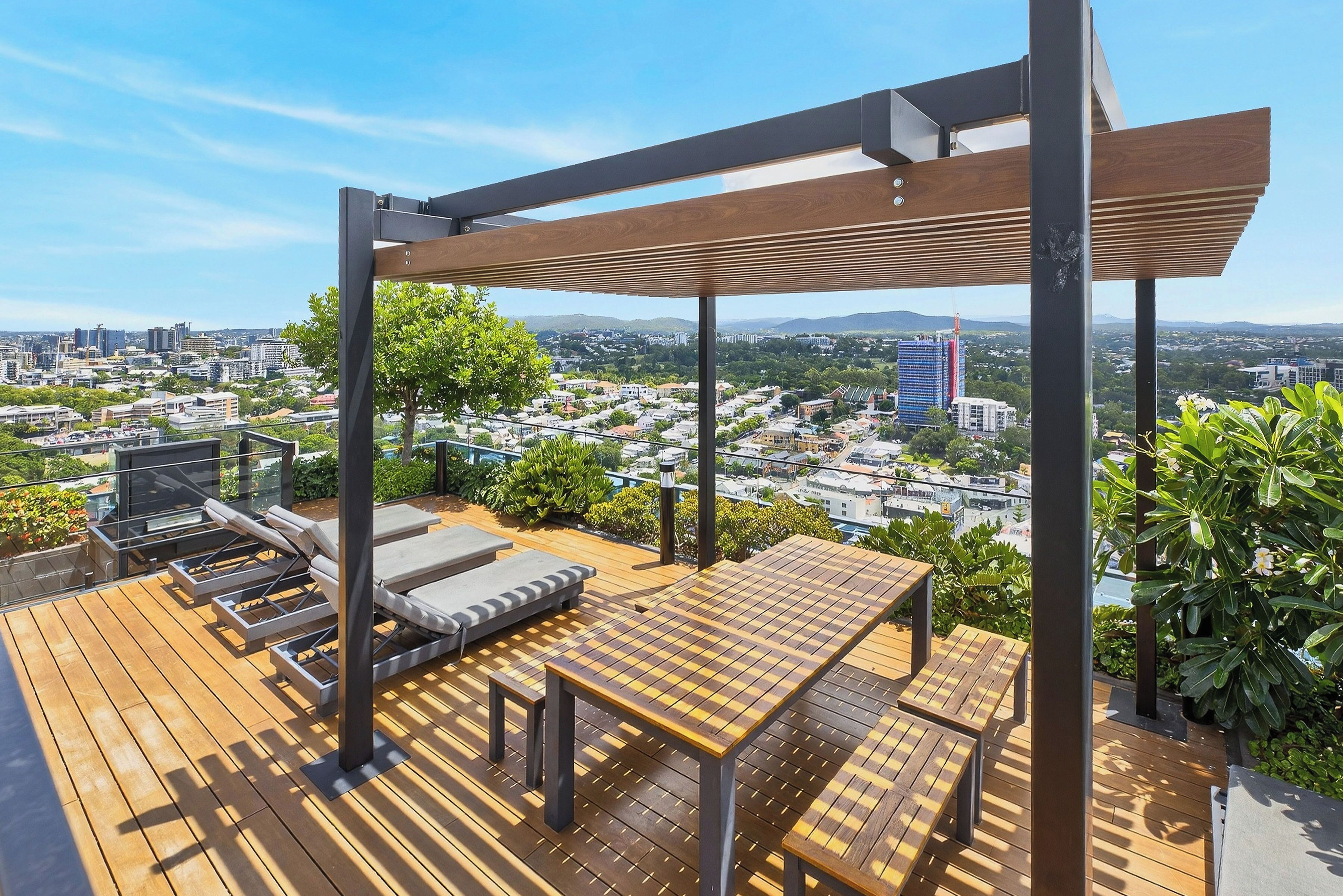 A rooftop terrace with a wooden deck, lounge chairs, and a table.