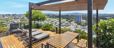 A rooftop terrace with a wooden deck, lounge chairs, and a table.