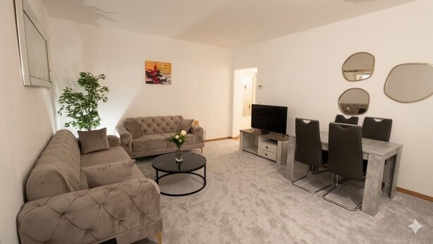 A living room with a sofa, a coffee table, a TV, and a dining area with chairs and a table. - Two bedrooms apartment with free underground parking place (Etterbeek)