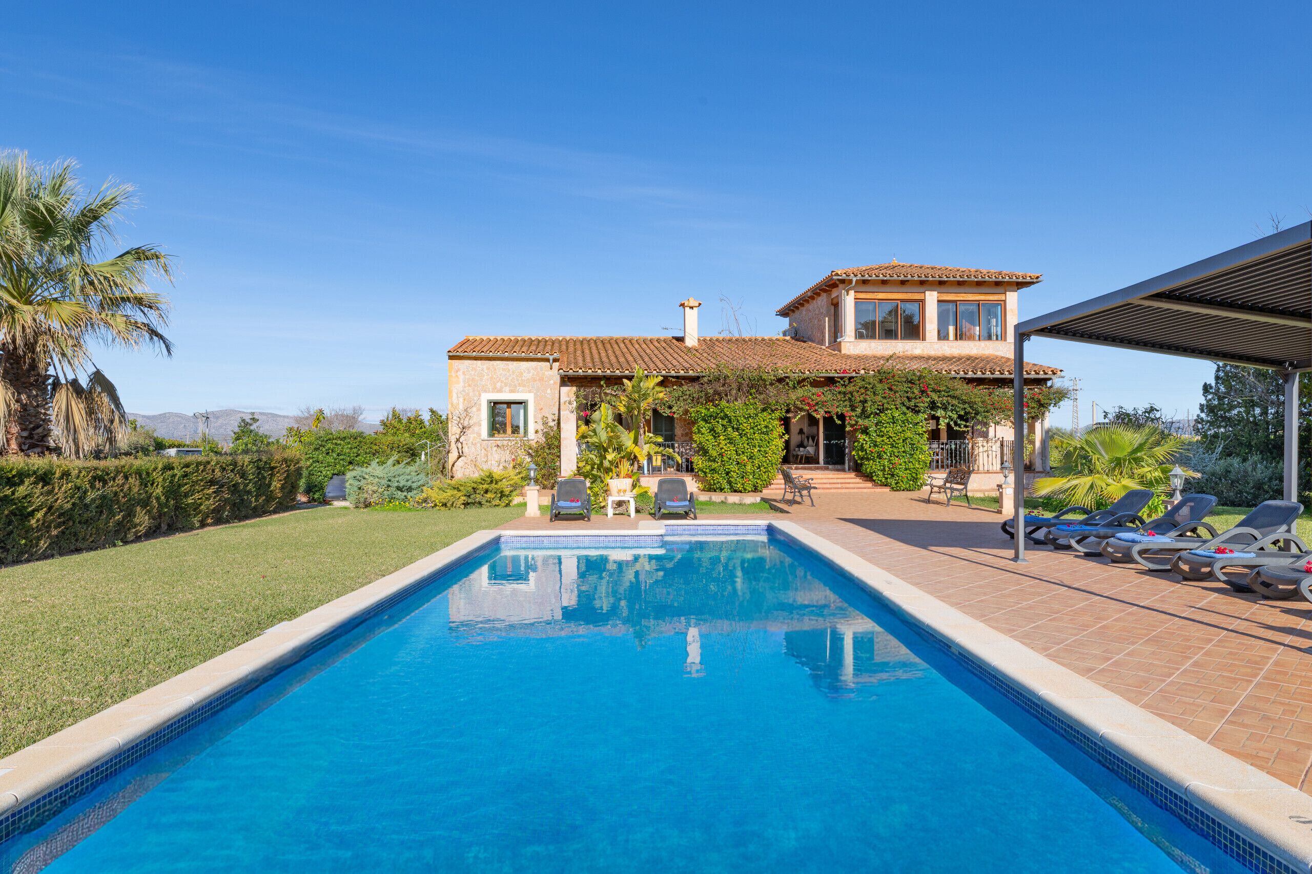 A swimming pool with lounge chairs and a house with a tiled roof.