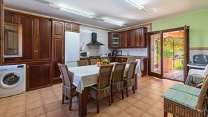 Une cuisine avec des meubles en bois, une table à manger avec des chaises, un lave-linge et une vue sur l’extérieur.