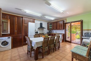 A kitchen with wooden cabinets, a dining table with chairs, a washing machine, and a view to the outside. - Can Torretes by Rentallorca (Alcúdia)