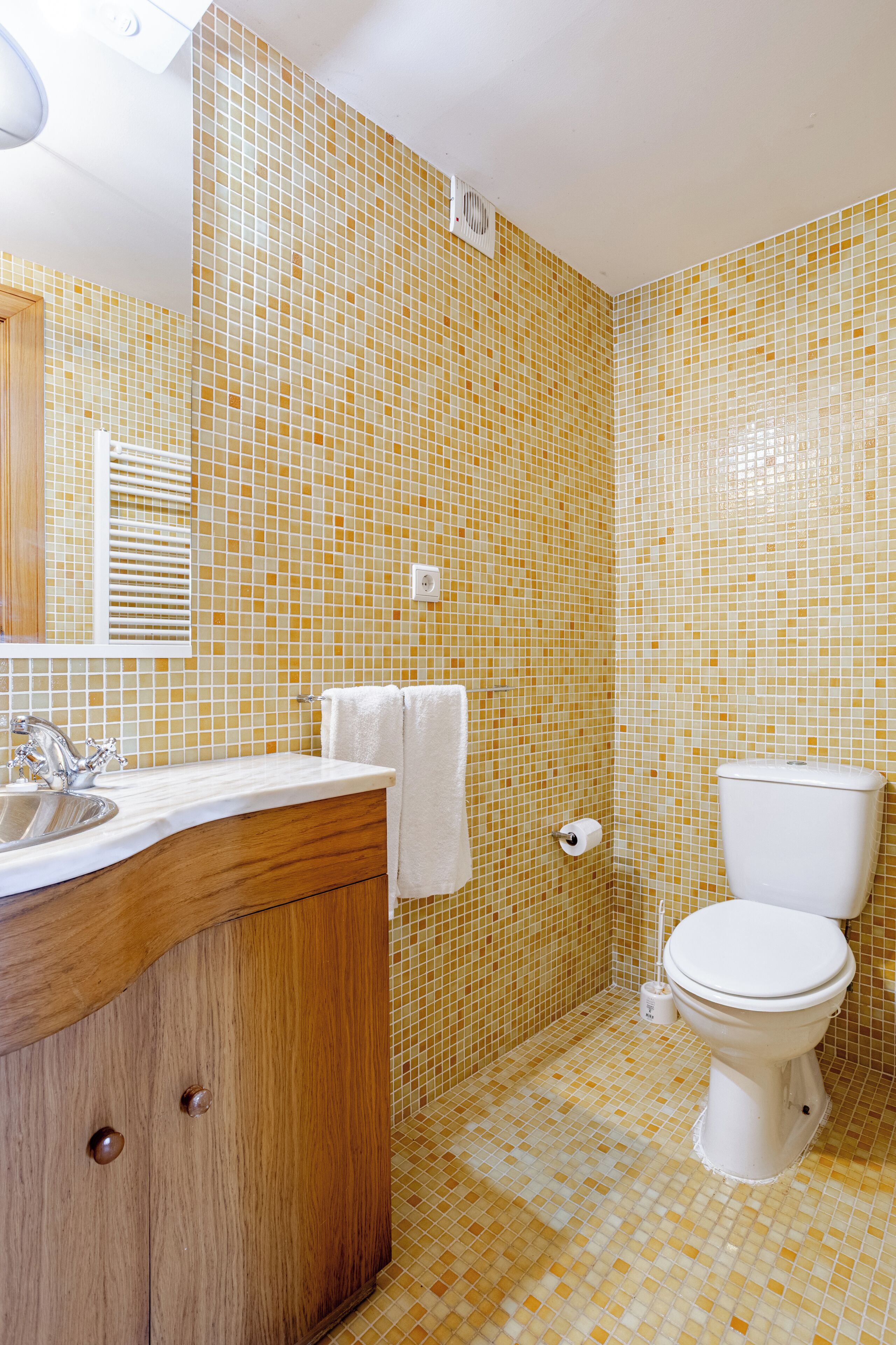Une salle de bain avec un sol carrelé, un meuble-lavabo en bois avec un évier, un miroir et des toilettes.