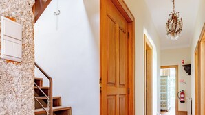 Un pasillo con suelo de madera, una escalera con barandillas de metal y un candelabro.