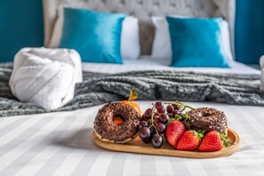 Un lit avec une couette blanche et un oreiller bleu, un plateau en bois avec deux beignets au chocolat et des fraises, et une serviette blanche sur le lit.