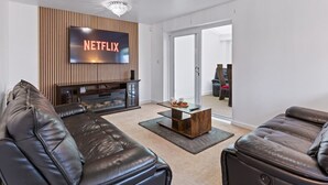 Un salon moderne avec des canapés en cuir, un mur d’accent en bois, un téléviseur à écran plat et une cheminée.