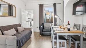 A modern living room with a sofa, a dining table set for two, and a kitchen in the background. - The Crews Quarters Anfield - Sleeps 10 - Modern (Merseyside)