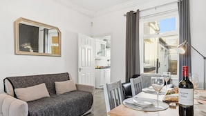 A modern living room with a sofa, dining table, and a wine bottle. - The Crews Quarters Anfield - Sleeps 10 - Modern (Merseyside)