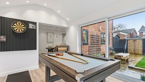 A pool table in a modern room with a dartboard, a bookshelf, and a view of a backyard.